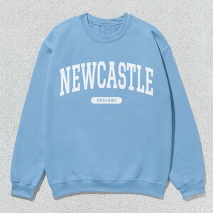 K&ouml;nnte beinhalten: Ein hellblauer Pullover mit wei&szlig;em Text, der "NEWCASTLE ENGLAND" lautet.