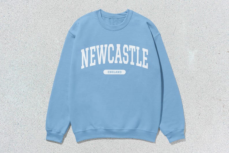 K&ouml;nnte beinhalten: Ein hellblauer Pullover mit wei&szlig;em Text, der "NEWCASTLE ENGLAND" lautet.