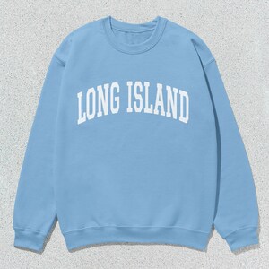 Pu&ograve; includere: Felpa azzurra con la scritta bianca "LONG ISLAND" in caratteri arcuati. La maglia a maniche lunghe ha lo scollo tondo ed &egrave; di colore uniforme. Il tessuto sembra morbido e confortevole.