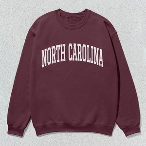 Pu&ograve; includere: Una felpa color bordeaux con la scritta "NORTH CAROLINA" stampata in bianco sul davanti.