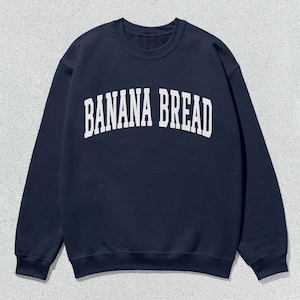 May include: A navy blue sweatshirt with the text "BANANA BREAD" in white letters across the front.