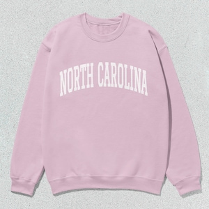 Pu&ograve; includere: Una felpa rosa con la scritta "NORTH CAROLINA" in bianco.