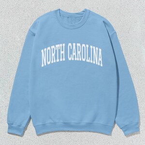 Pu&ograve; includere: Una felpa blu chiaro con la scritta "NORTH CAROLINA" stampata in bianco sul davanti.
