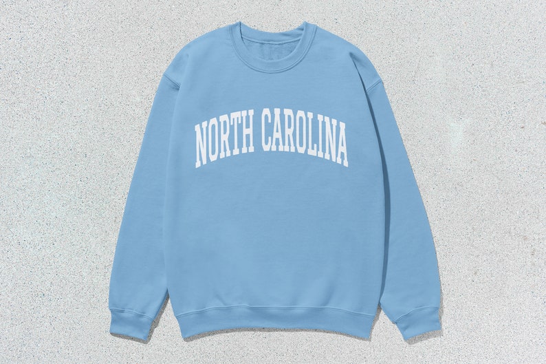 Pu&ograve; includere: Una felpa blu chiaro con la scritta "NORTH CAROLINA" stampata in bianco sul davanti.