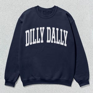 May include: Navy blue sweatshirt with the white text "DILLY DALLY" in a collegiate font across the chest. The long-sleeved crewneck top is made of a soft material and is suitable for casual wear.