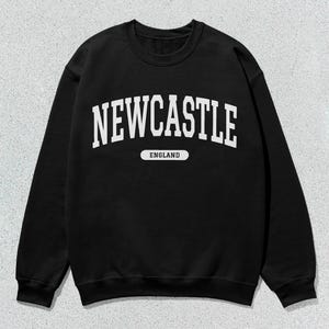 K&ouml;nnte beinhalten: Schwarzer Pullover mit wei&szlig;em Text, der "NEWCASTLE ENGLAND" in einer College-Schriftart lautet.