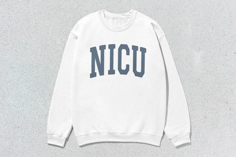 Puede incluir: Sudadera blanca de cuello redondo con la palabra "NICU" impresa en letras azules en el pecho. La sudadera tiene mangas largas y un cuello acanalado.