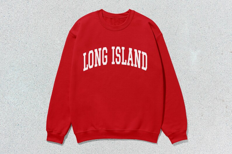 Pu&ograve; includere: Una felpa rossa con la scritta bianca "LONG ISLAND" in caratteri arcuati. La felpa ha un girocollo e maniche lunghe. L'immagine &egrave; ambientata su uno sfondo grigio maculato.