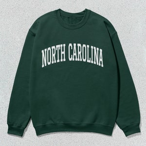 Pu&ograve; includere: Una felpa verde scuro con la scritta "NORTH CAROLINA" in lettere bianche sul davanti.