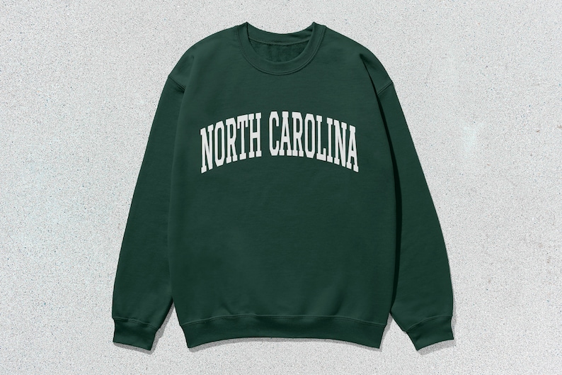 Pu&ograve; includere: Una felpa verde scuro con la scritta "NORTH CAROLINA" in lettere bianche sul davanti.