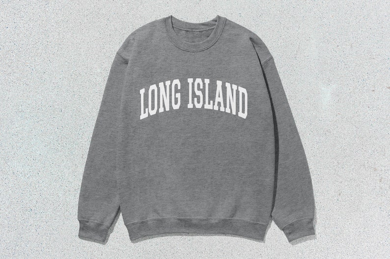 Pu&ograve; includere: Una felpa grigia con la scritta "LONG ISLAND" in bianco, a lettere arcuate. La felpa girocollo &egrave; realizzata in un materiale morbido ed &egrave; adatta per un abbigliamento casual. L'immagine &egrave; scattata su uno sfondo strutturato grigio chiaro.