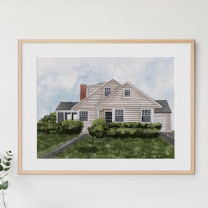 May include: Watercolor painting of a house with a light brown exterior, a red brick chimney, and a dark gray roof. The house is surrounded by green bushes and a cloudy sky. The artwork is framed in a light brown wooden frame.