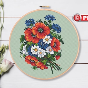 May include: Cross stitch pattern of a bouquet of red poppies, white daisies, and blue cornflowers on a green background. The pattern is in a round embroidery hoop.