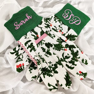 Peut inclure: Une paire de gants de jardinage blancs avec un motif floral vert. Les gants ont des poignets verts avec des noms brod&eacute;s en rose "Sarah" et "S.D."