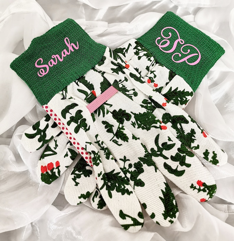 Peut inclure: Une paire de gants de jardinage blancs avec un motif floral vert. Les gants ont des poignets verts avec des noms brod&eacute;s en rose "Sarah" et "S.D."