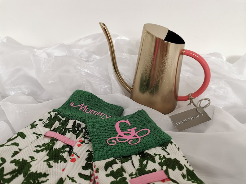 Peut inclure: Une paire de gants de jardinage verts avec un imprim&eacute; floral rose et des lettres brod&eacute;es roses. Les gants disent "Mummy" et "G". Un arrosoir dor&eacute; avec une poign&eacute;e rose est en arri&egrave;re-plan.