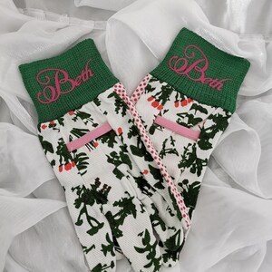 Peut inclure: Une paire de gants de jardinage blancs avec un poignet vert et des pois roses. Les poignets sont brod&eacute;s du nom "Beth" en rose.