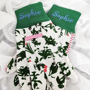 Peut inclure: Une paire de gants de jardinage blancs avec un poignet vert et un motif floral. Les poignets sont personnalis&eacute;s avec le nom "Sophie" en lettres bleues.