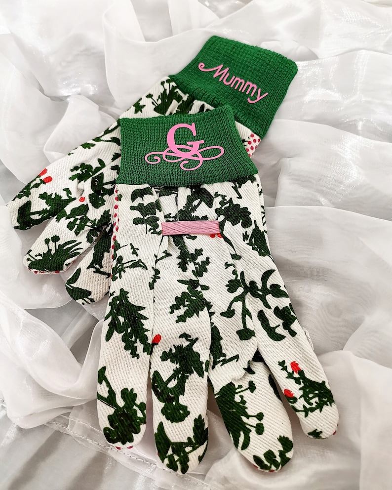Peut inclure: Une paire de gants de jardinage blancs avec un motif floral vert et blanc. Les gants ont un poignet vert avec la lettre "G" brod&eacute;e en rose. L'autre poignet est vert et dit "Mummy" en rose.