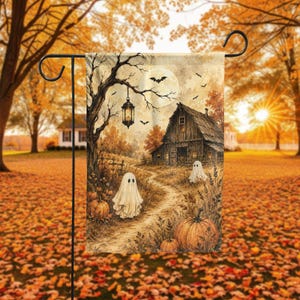 May include: A rectangular garden flag featuring a sepia-toned illustration of a rustic barn, a winding path, and two white ghost figures. The scene includes orange pumpkins, a hanging lantern from a bare tree, and bats flying under a full moon.