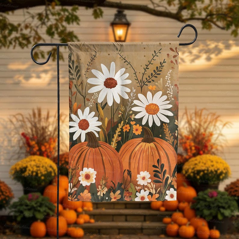 Puede incluir: Una bandera de jard&iacute;n decorativa con tem&aacute;tica oto&ntilde;al. La bandera muestra dos grandes calabazas naranjas, margaritas blancas con centros marrones y varias hojas de oto&ntilde;o. El fondo es de color beige apagado y la bandera est&aacute; colgada de un soporte de metal negro.