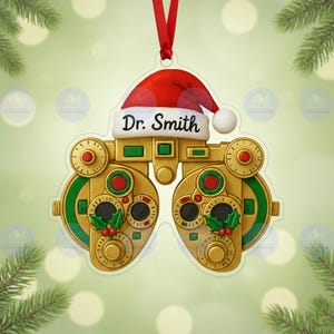 Puede incluir: Adorno navideño con forma de máquina de examen ocular, coronado por un gorro de Papá Noel rojo. El gorro muestra el nombre "Dr. Smith". El adorno es dorado y verde con detalles rojos, y tiene una cinta roja para colgar.
