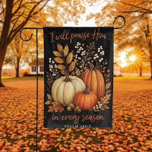 May include: A rectangular garden flag with a black background featuring three pumpkins in white and orange, surrounded by autumn leaves and white berries. The text reads "I will praise Him in every season" and "PSALM 146:2" in a cursive font.