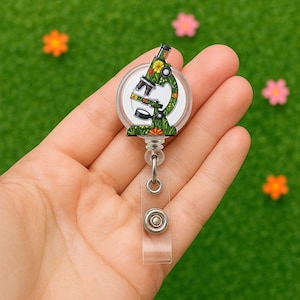 May include: A green and floral patterned microscope design on a clear plastic retractable badge reel. The reel has a silver metal clip and a silver metal button.
