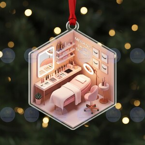 以下が含まれることがあります： 六角形のクリスマスオーナメント。ミニチュアのまつげスタジオが描かれています。内部にはピンク色の施術ベッド、椅子、鏡、美容製品が置かれた棚があります。「Megan's Lash Studio」の文字が見えます。