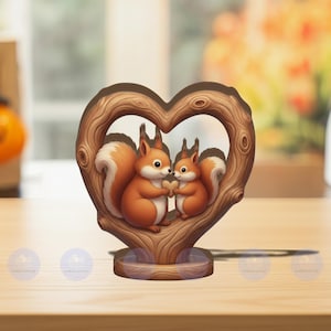 Könnte beinhalten: Holzdekoration in Herzform mit zwei Cartoon-Eichhörnchen mit orangefarbenem Fell und weißen Schwänzen, die eine herzförmige Nuss halten. Die Eichhörnchen befinden sich in einem braunen Holzrahmen. Der Sockel ist hellbraun.