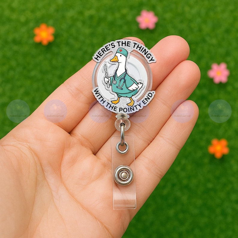May include: A clear badge reel with a cartoon duck wearing a medical uniform and holding a scalpel. The text on the badge reel reads "HERE'S THE THINGY WITH THE POINTY END."