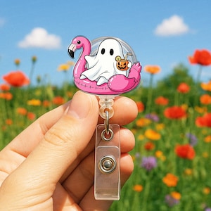 Könnte beinhalten: Ein Halloween-Badge-Roller mit einem Cartoon-Geist, der in einem rosa Flamingo-Pool-Float schwimmt. Der Geist hält einen Cocktail mit einem Kürbisgesicht. Der Badge-Roller hat einen transparenten Kunststoffclip und ein einziehbares Kabel.