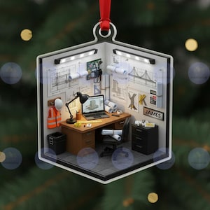 May include: A Christmas ornament shaped like a room, depicting an engineer's office. The ornament features a desk with a laptop, blueprints, and a nameplate that reads "JAMES". It includes a hard hat, safety vest, and a black office chair.