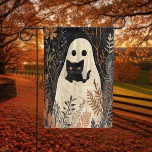 May include: A Halloween garden flag featuring a white ghost holding a black cat. The flag has a black background with floral and plant illustrations in shades of brown, beige, and green. The flag is displayed on a black metal garden stake.