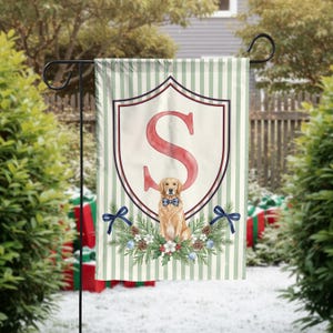 May include: A garden flag featuring a light green and white vertical striped background. A large red letter S is centered within a shield outline. Below the letter, a golden retriever wearing a blue plaid bowtie sits amidst pine branches, pinecones, and blue ribbons.