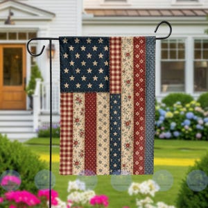 May include: A garden flag featuring a patchwork design of the American flag. The flag has a navy blue field with white stars and alternating red and white stripes with floral and polka dot patterns. The flag is displayed on a black metal stand.