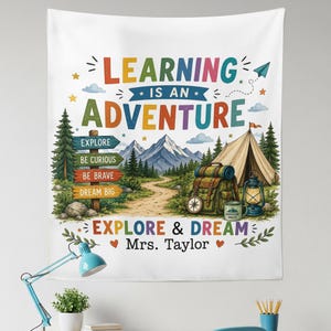 May include: A white wall tapestry featuring a colorful mountain landscape with a tent, backpack, lantern, and a signpost. The text reads: LEARNING IS AN ADVENTURE, EXPLORE, BE CURIOUS, BE BRAVE, DREAM BIG, EXPLORE & DREAM, and Mrs. Taylor.