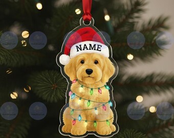 May include: A clear acrylic Christmas ornament shaped like a golden retriever puppy wearing a Santa hat with the word "NAME" on it. The puppy is wrapped in a string of colorful Christmas lights and hangs from a red ribbon.