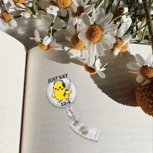 Könnte beinhalten: Ein durchsichtiger, ausziehbare Badgehalter aus Plastik mit einem gelben Küken, das ein Messer hält und Kopfhörer trägt. Der Text "JUST SAY 10-4" ist auf dem Badgehalter aufgedruckt.