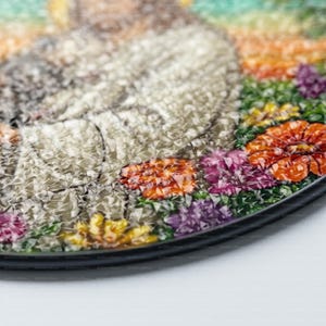 May include: Close-up of a round, colorful mosaic art piece with a floral design. The mosaic is made of small, colorful glass tiles and features a variety of flowers, including red, orange, yellow, purple, and green. The mosaic is set in a black frame.