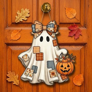May include: A decorative ghost wall hanging featuring a large plaid bow at the top and various fabric-style patches in orange, brown, and grey patterns. The ghost holds a jack-o'-lantern bucket filled with autumn leaves and small pumpkins.