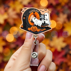May include: A badge reel featuring an acrylic topper with a Halloween-themed illustration of a ghost lying in a radiology CT scanner while another ghost holds an X-ray. The design includes orange pumpkins, black bats, and the text RADIOLOGY.