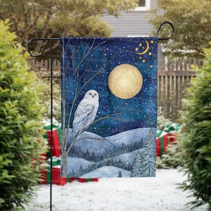 May include: A garden flag featuring a snowy owl perched on a tree branch, set against a night sky with a full moon and stars. The design includes a winter landscape with snow-covered hills and evergreen trees. The flag is displayed on a black metal stand.