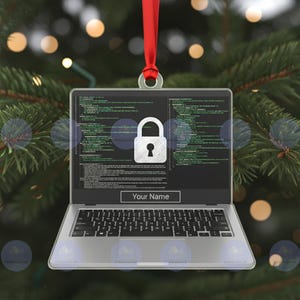 Puede incluir: Adorno navideño de portátil plateado con una cinta roja. La pantalla del portátil muestra líneas de código y un icono de candado blanco. El texto "Your Name" está debajo. El adorno cuelga frente a un árbol de Navidad borroso.
