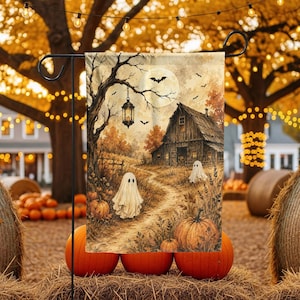 May include: A rectangular garden flag featuring a Halloween scene with two white ghosts, orange pumpkins, a rustic wooden barn, a hanging lantern, and a full moon in a tree-lined landscape. The artwork displays a warm autumn color palette.