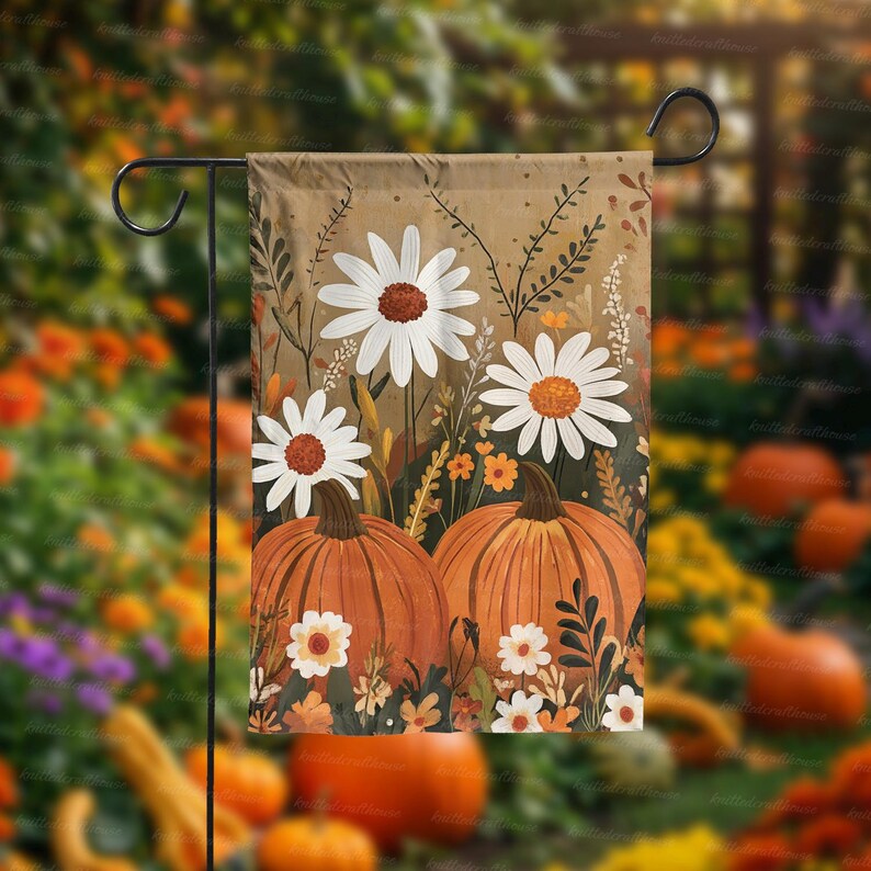 Puede incluir: Una bandera de jard&iacute;n con un dise&ntilde;o de cosecha de oto&ntilde;o. La bandera muestra dos calabazas naranjas y margaritas blancas con centros marrones. El fondo es una mezcla de marr&oacute;n y verde, con elementos florales adicionales.