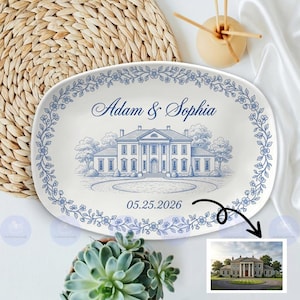 May include: Oval ceramic platter featuring a blue and white illustration of a grand house, floral border, and the names "Adam & Sophia" with the date "05.25.2026". The platter is surrounded by a woven mat and a succulent plant.