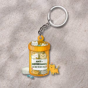 May include: A novelty keychain featuring a pill bottle design with the words "ANTI-DEPRESSANTS" and "TAKE DAILY FOR BEST RESULTS." The bottle is filled with cartoon cats. Includes a silver keyring and chain.