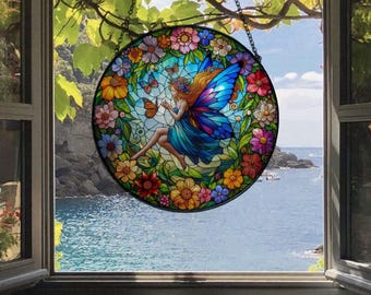 May include: A stained glass window hanging depicts a colourful fairy with blue wings and a floral design. The fairy is surrounded by butterflies and flowers in shades of pink, yellow, orange, and green.