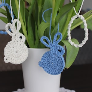 Könnte beinhalten: Zwei gehäkelte Hasen-Anhänger, die an einem Strauß grüner Tulpen hängen. Ein Hase ist weiß und der andere ist blau.